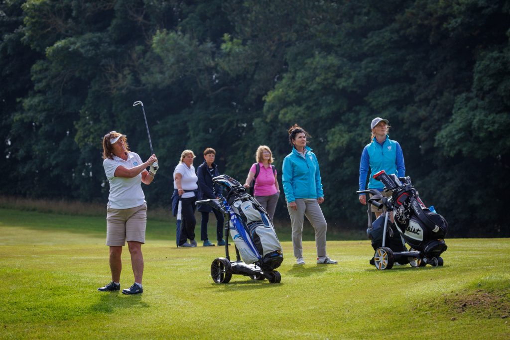 Sekelompok pegolf dan penonton wanita menyaksikan anggota tim Galloway Ladies memainkan bolanya di Final Wilayah Wanita di Klub Golf Kirkcaldy. 